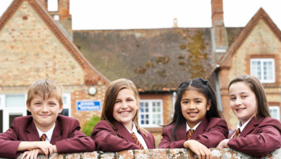 Four school kids in uniform leaning on a wall smiling