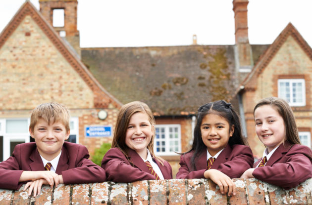 Four school kids in uniform leaning on a wall smiling