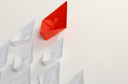 A red paper boat leading a flock of white paper boats