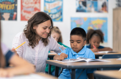 Teacher sitting beside student's desk helping him with classwork