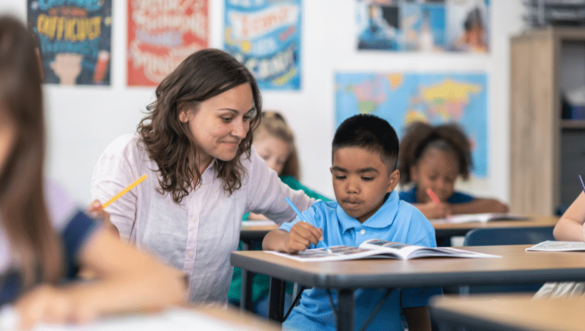 Teacher sitting beside student's desk helping him with classwork